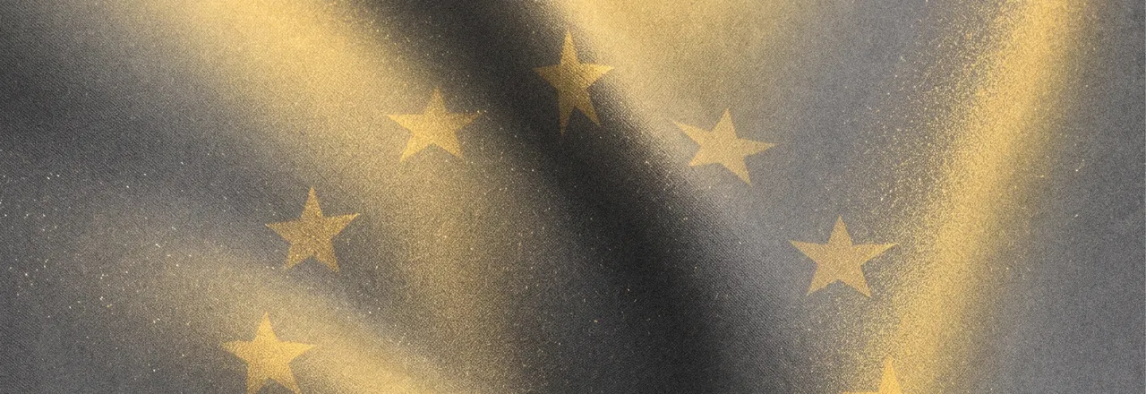 Close-up of the European flag as fabric, its golden stars catching raking light on dark grey cloth