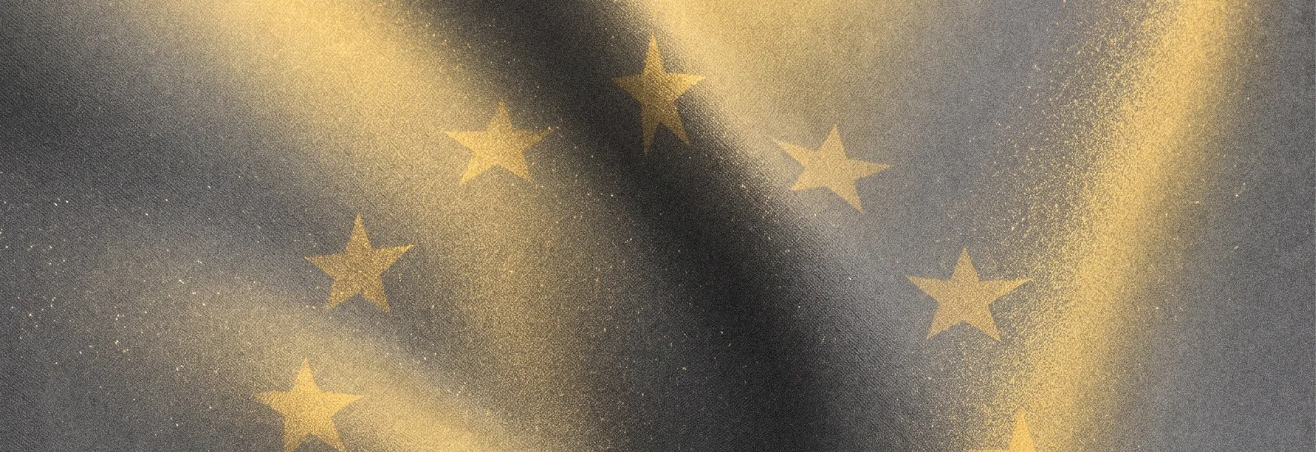 Close-up of the European flag as fabric, its golden stars catching raking light on dark grey cloth