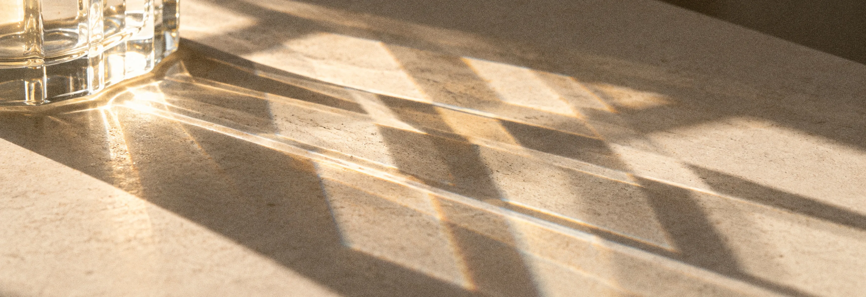 Low sunlight through a window casting a grid of soft shadows across a pale travertine surface
