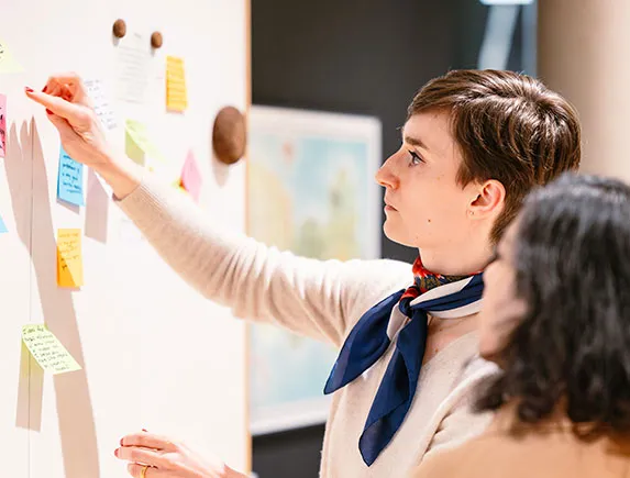 Teilnehmerin klebt Haftnotizen an ein Whiteboard während einer Workshop-Session bei einem Team-Event.